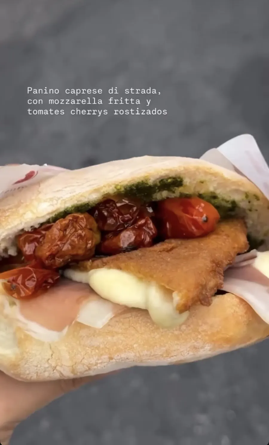 Panino caprese abierto con mozzarella fritta derretida, tomates cherry rostizados y pesto, sostenido en la calle