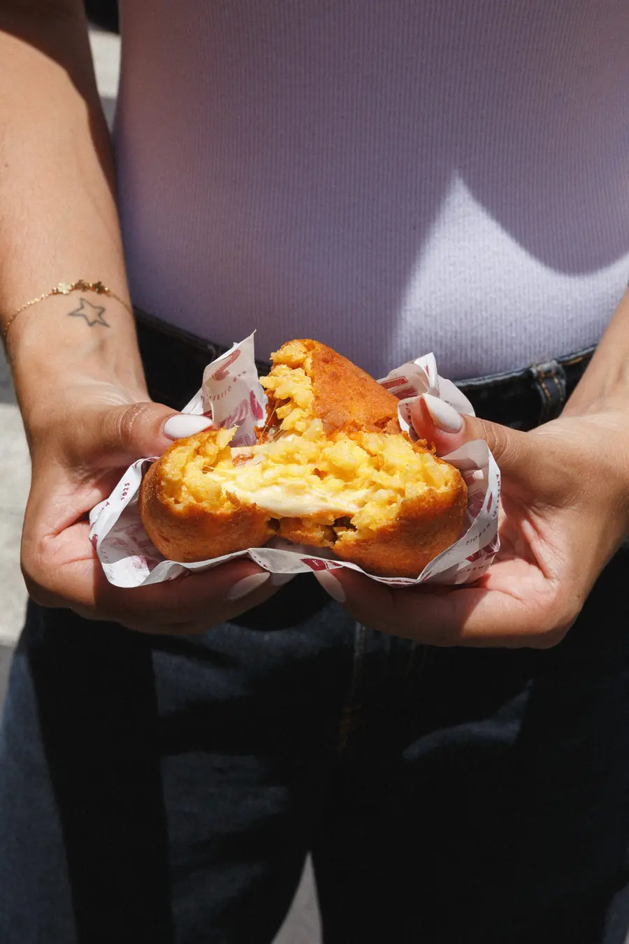 Panzerotto frito partido por la mitad, con el relleno de queso derretido a la vista, sostenido con las dos manos